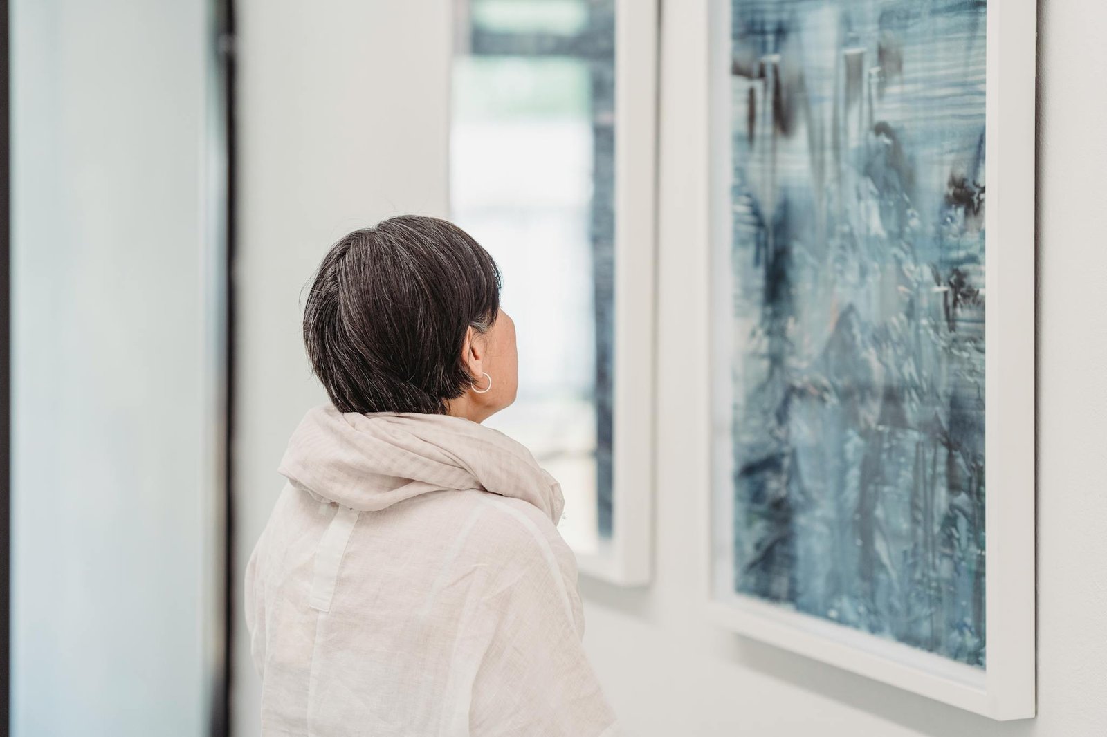 A woman studies a blue abstract painting in a modern art gallery.